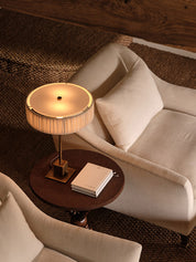 Small round table with a lamp and book next to a beige sofa on a wooden floor.