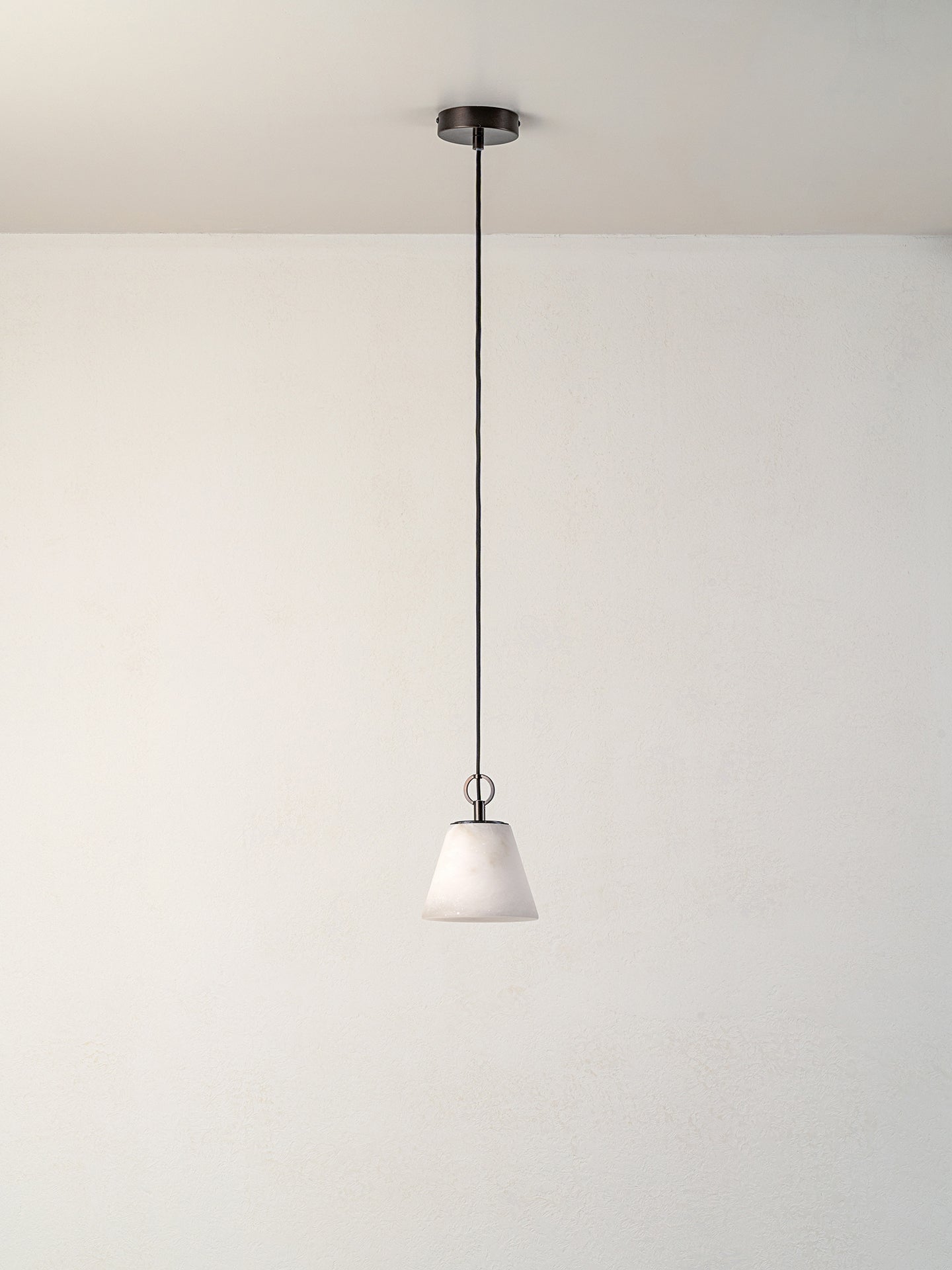 A modern pendant light with a white tapered glass shade and a dark metal canopy and cord, suspended against a plain white wall and ceiling.