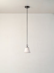A modern pendant light with a white tapered glass shade and a dark metal canopy and cord, suspended against a plain white wall and ceiling.