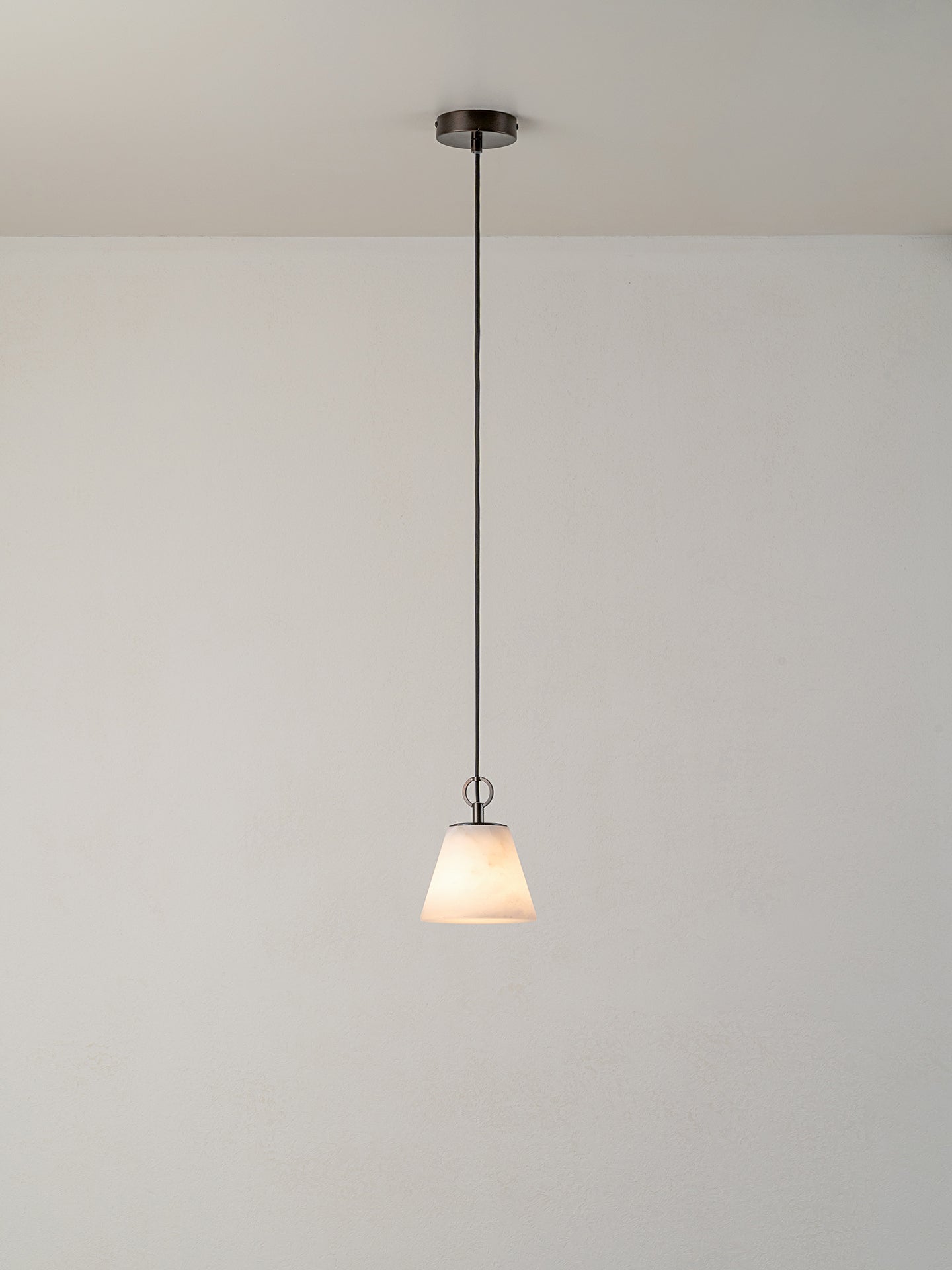 A modern pendant light with a white tapered glass shade and a dark metal canopy and cord, suspended against a plain white wall and ceiling.