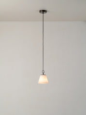 A modern pendant light with a white tapered glass shade and a dark metal canopy and cord, suspended against a plain white wall and ceiling.