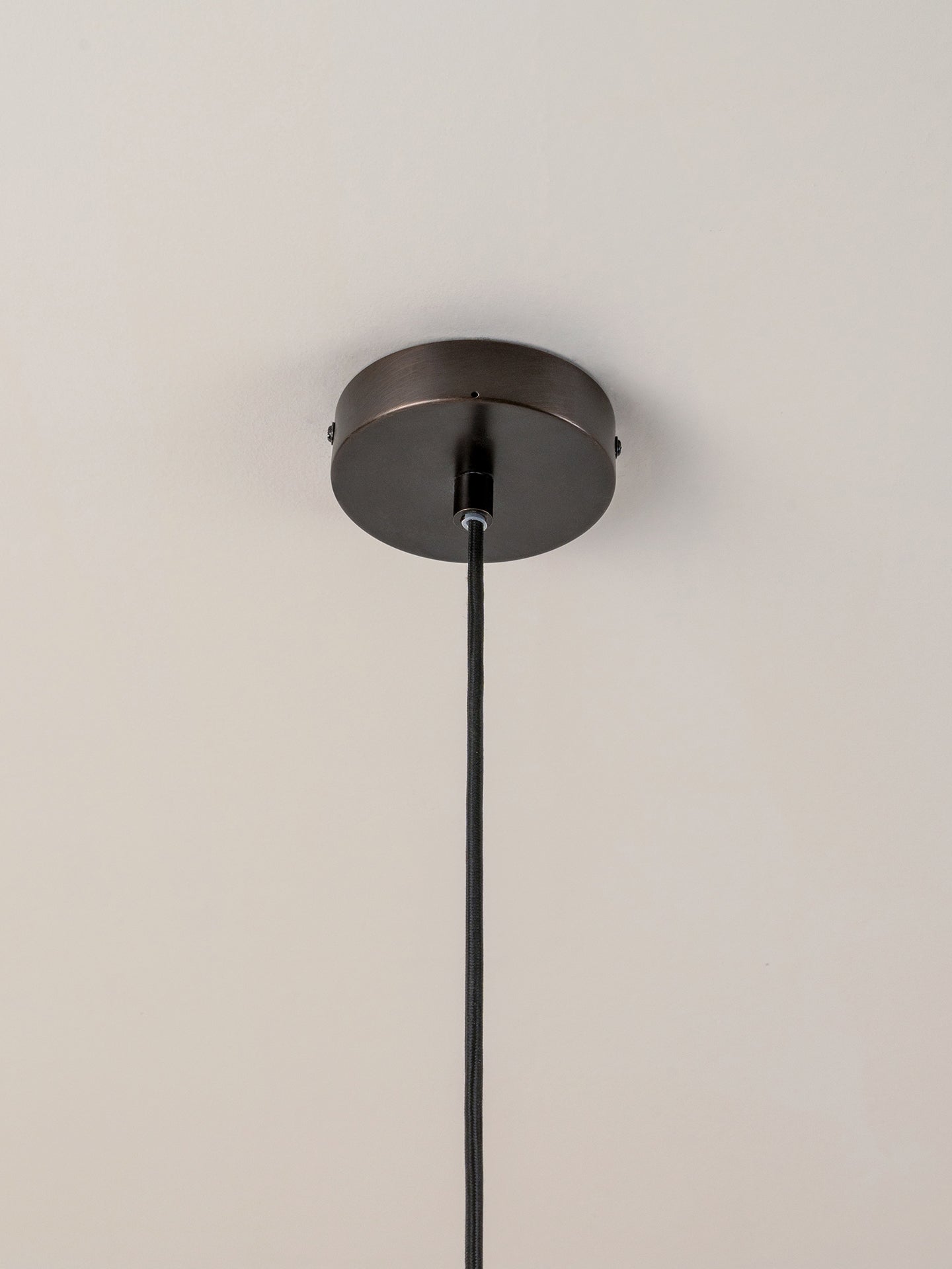  dark metal canopy and cord, suspended against a plain white wall and ceiling.