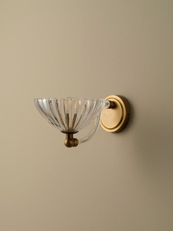Wall-mounted light fixture with glass shade and gold finish on a beige wall.