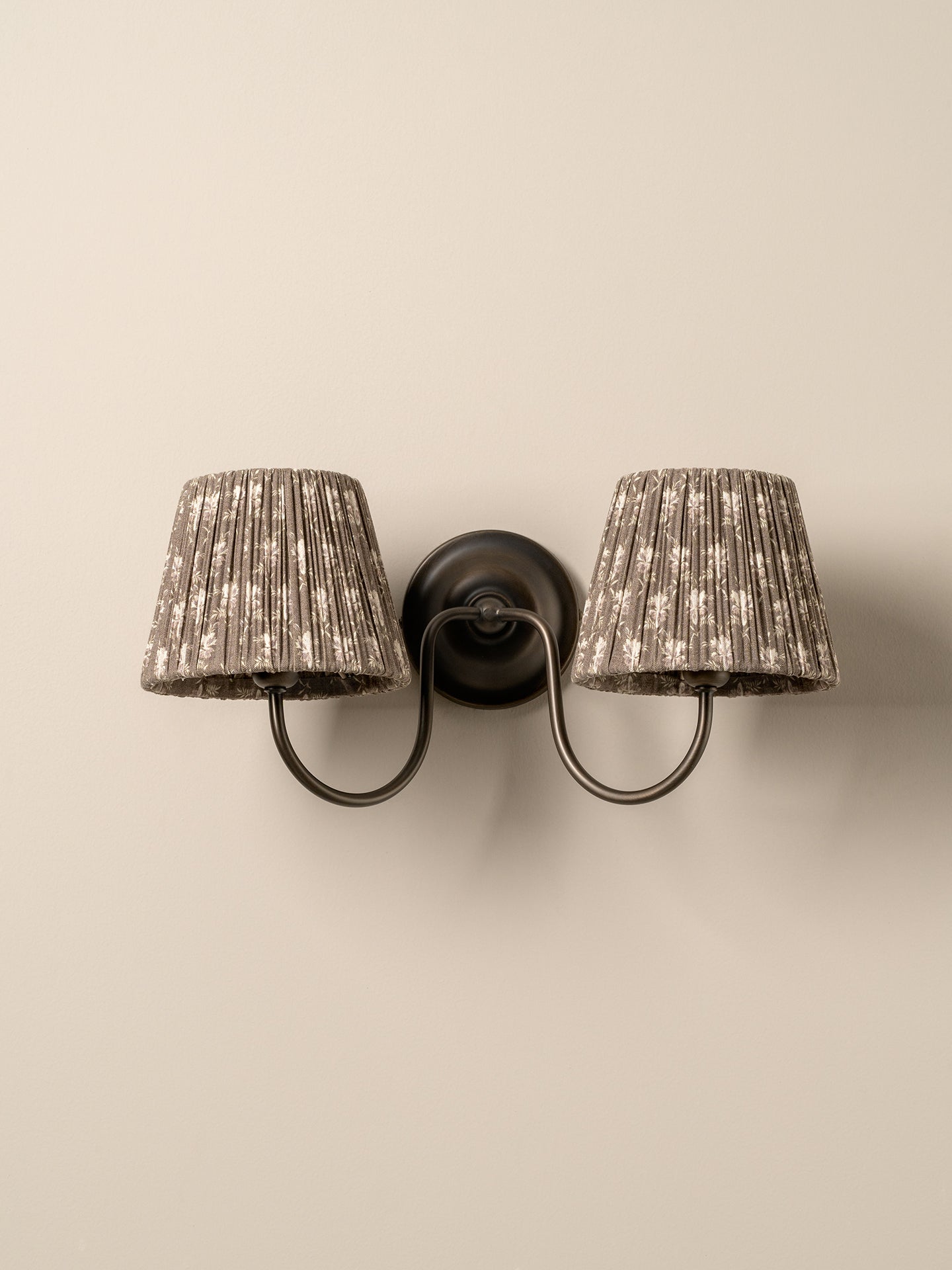 A two-light wall sconce with textured, pleated drum shades in a speckled beige and gray pattern, mounted on a dark metal wall bracket with curved arms.