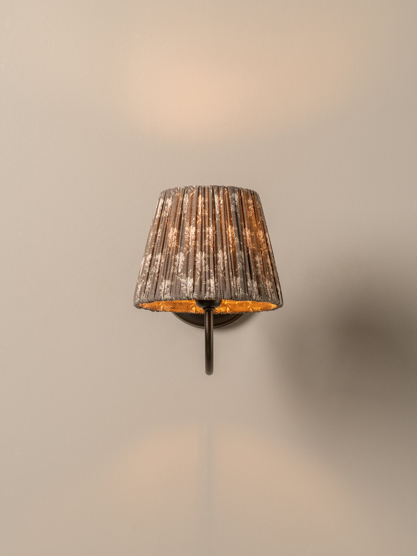 A wall-mounted sconce with a pleated fabric shade in a distressed gray and white pattern, mounted on a dark metal bracket against a plain beige wall.
