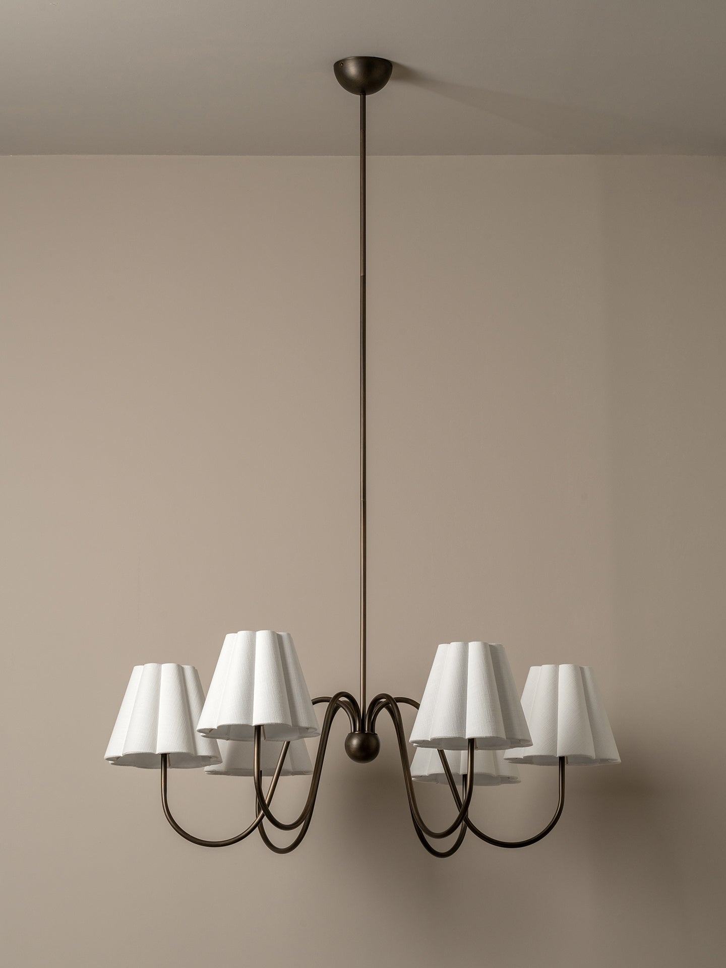 A six-light chandelier with white tapered fabric shades and a dark metal frame, suspended from a ceiling against a beige wall.