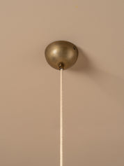 A close-up of a ceiling-mounted pendant light fixture with a brushed brass or bronze spherical ceiling canopy and a white cord extending downward against a warm beige wall.