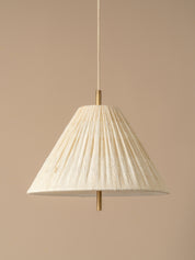 A cream pleated fabric pendant lampshade with a brass metal top and bottom finials, suspended by a matching cream cord against a solid beige background.