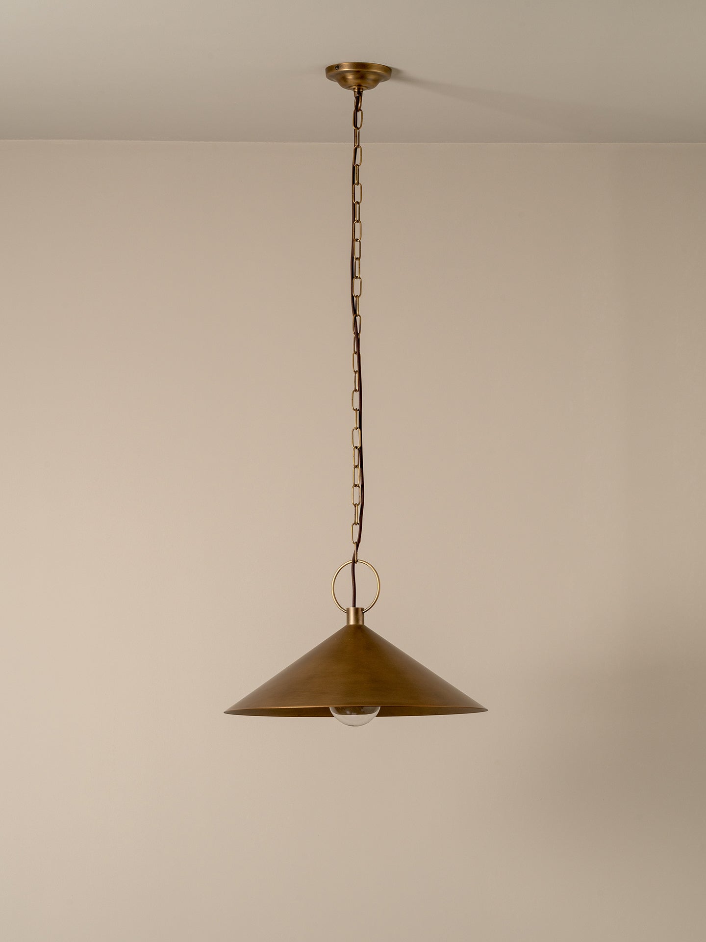 A single brass pendant light with a conical shade hanging from a chain against a plain beige wall.