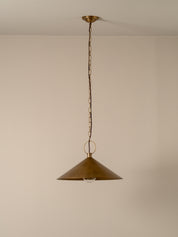 A single brass pendant light with a conical shade hanging from a chain against a plain beige wall.