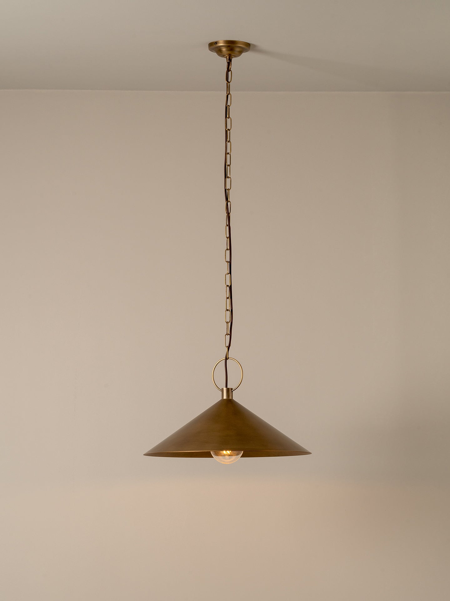 A single brass pendant light with a conical shade hanging from a chain against a plain beige wall and ceiling.