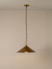 A single brass pendant light with a conical shade hanging from a chain against a plain beige wall and ceiling.