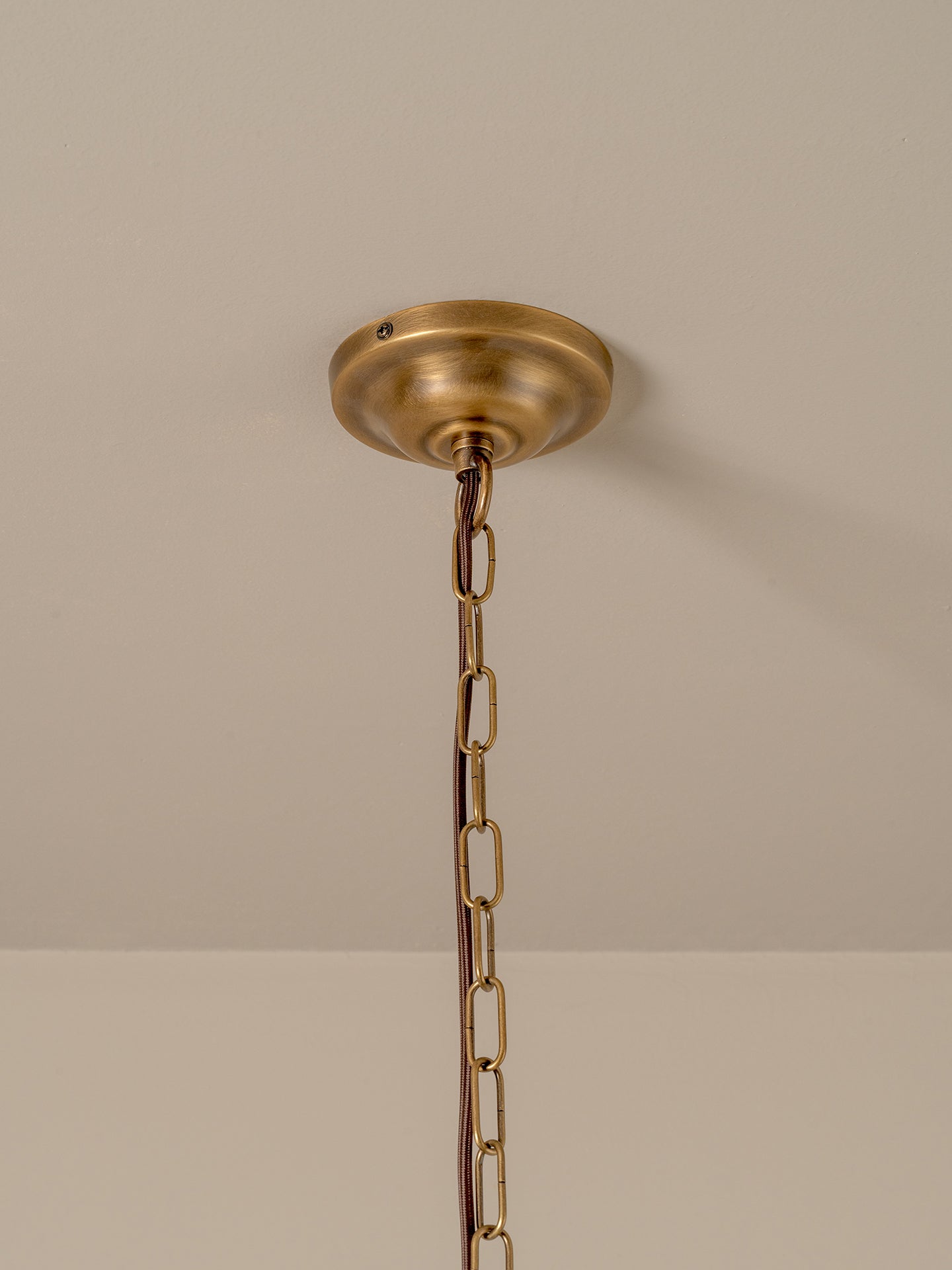A brass ceiling light fixture canopy and chain hanging against a plain beige wall and ceiling.