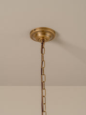 A brass ceiling light fixture canopy and chain hanging against a plain beige wall and ceiling.