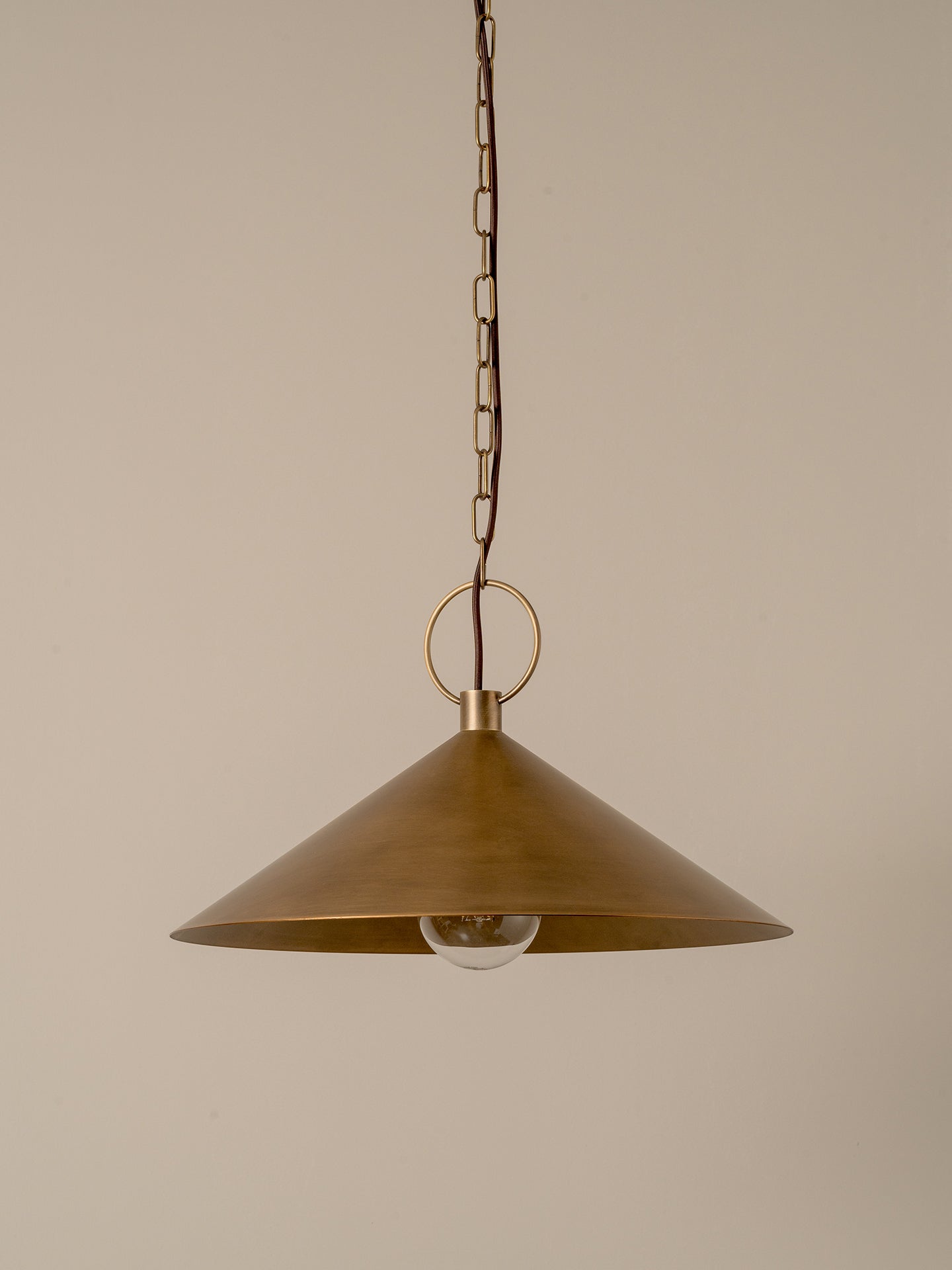 A brass pendant light with a wide conical shade, hanging from a chain against a plain beige background.