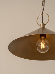A single brass pendant light with a conical shade hanging from a chain against a plain beige wall.