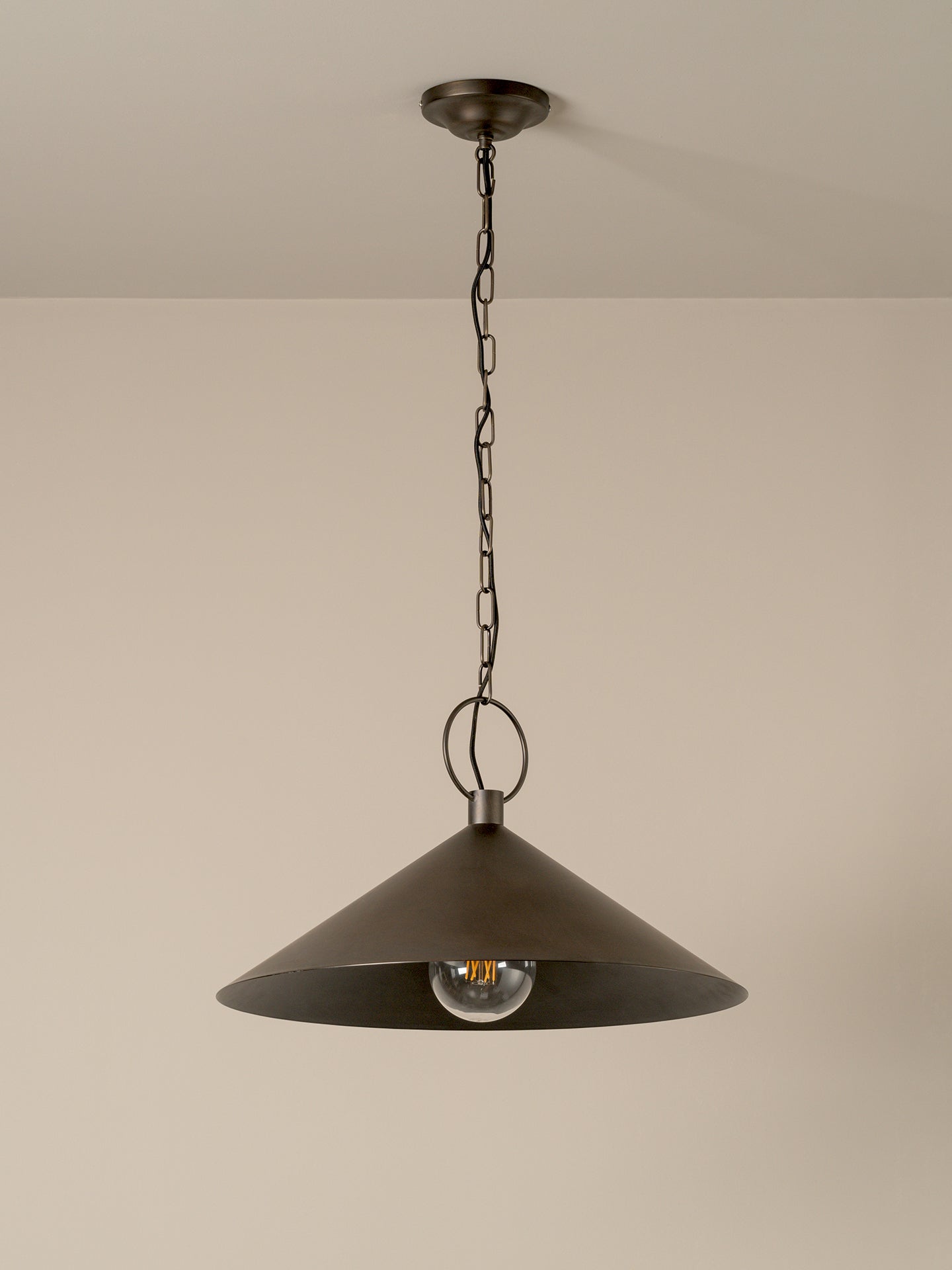 A dark bronze metal pendant light with a wide conical shade hanging from a chain against a plain beige wall.