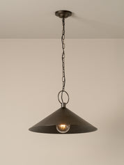 A dark metal pendant light with a wide conical shade hanging from a chain and ceiling canopy against a plain beige wall.