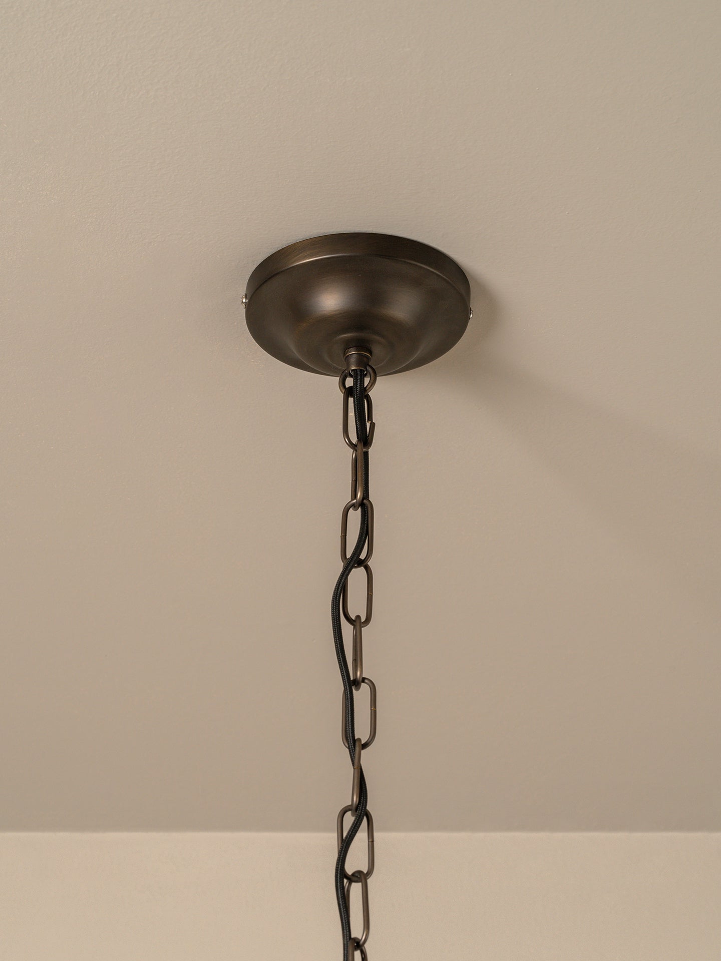 A dark bronze ceiling light fixture canopy hanging from a black metal chain against a beige textured ceiling.