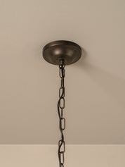 A dark bronze ceiling light fixture canopy hanging from a black metal chain against a beige textured ceiling.