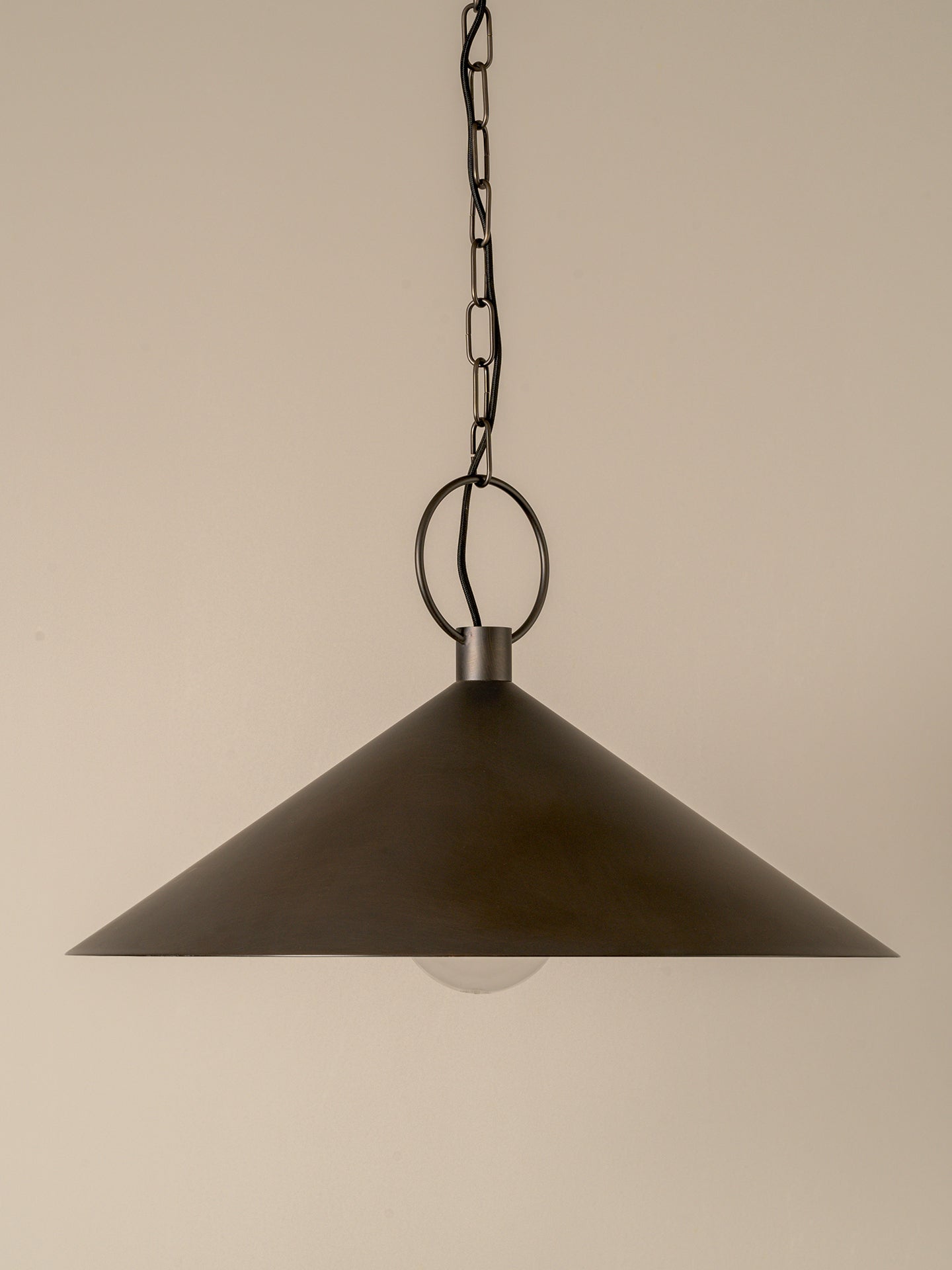 A dark metal cone-shaped pendant light hanging from a chain and ring against a plain beige background.
