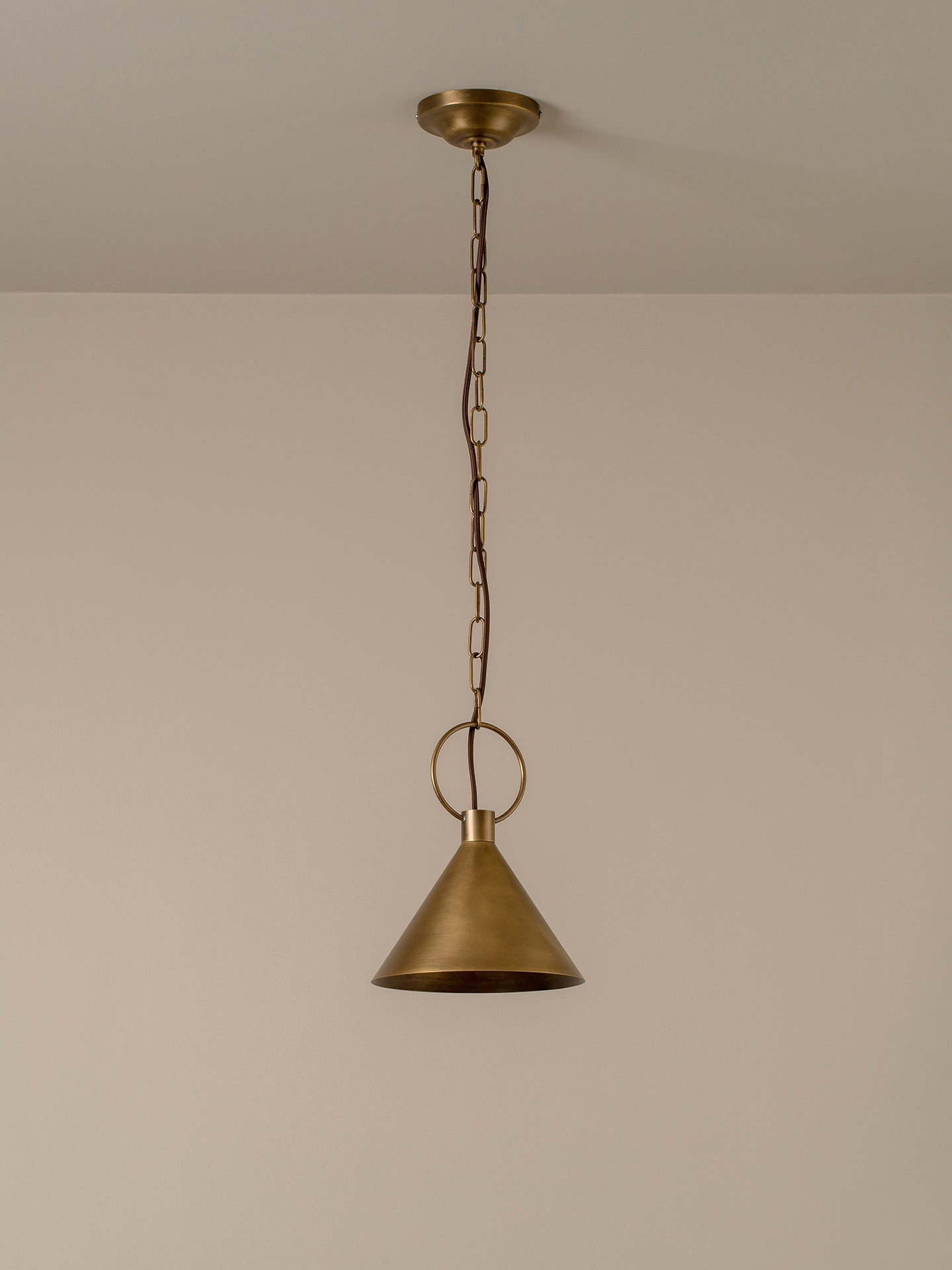 A single brass pendant light hanging from a ceiling with a chain and circular ring, shown against a plain beige wall.