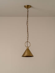A single brass pendant light hanging from a ceiling with a chain and circular ring, shown against a plain beige wall.
