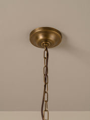 An antique brass ceiling canopy with a hanging chain, shown against a neutral beige wall.