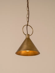 An industrial-style pendant light with a brushed brass cone shade and a visible warm Edison bulb inside, suspended by a circular ring against a plain beige background.