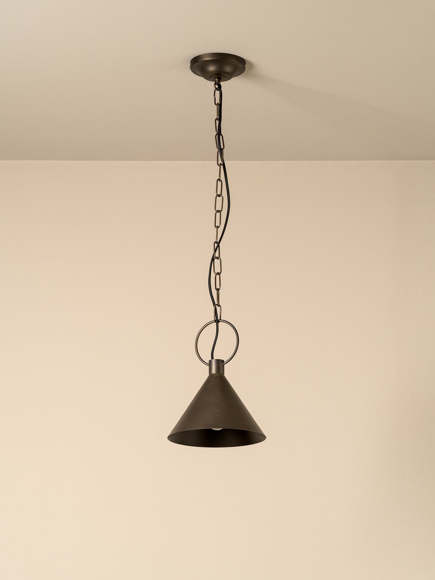 A single pendant light with a dark bronze metal shade and chain, hanging against a plain beige wall and ceiling.