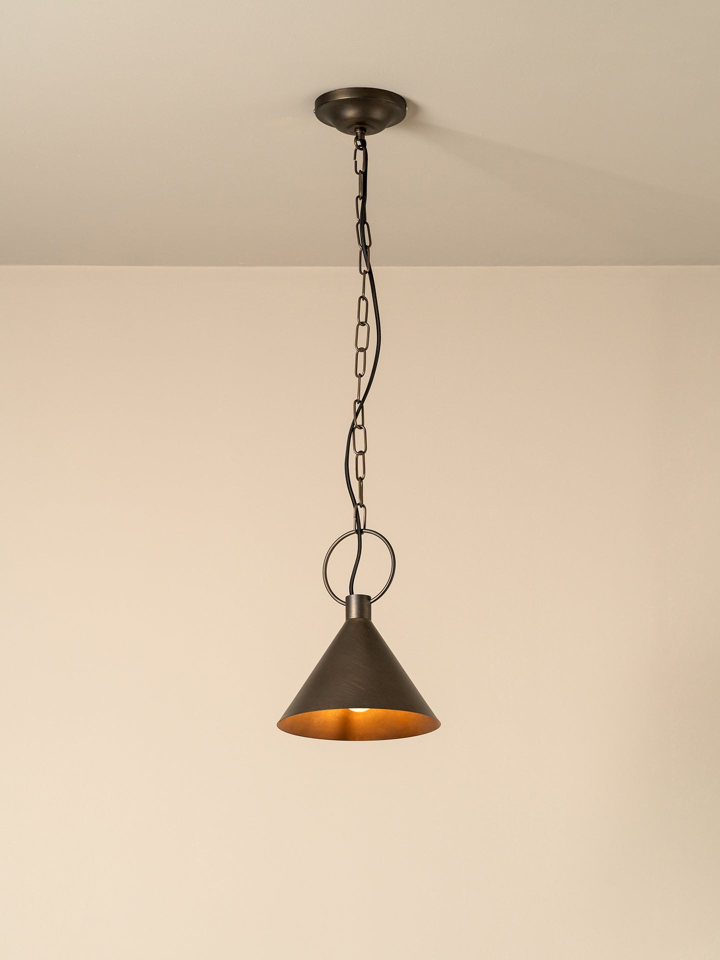 A single pendant light with a dark bronze metal shade and chain, hanging against a plain beige wall and ceiling.