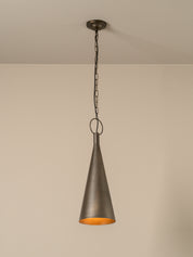 A single pendant light with a dark bronze metal cone shade and a warm orange-gold interior, hanging from a chain against a plain beige wall.