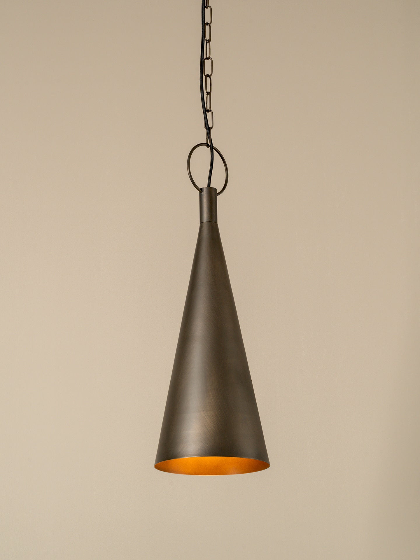 A single cone-shaped pendant light in a dark bronze finish with a warm orange-gold interior, hanging from a chain against a plain beige background.