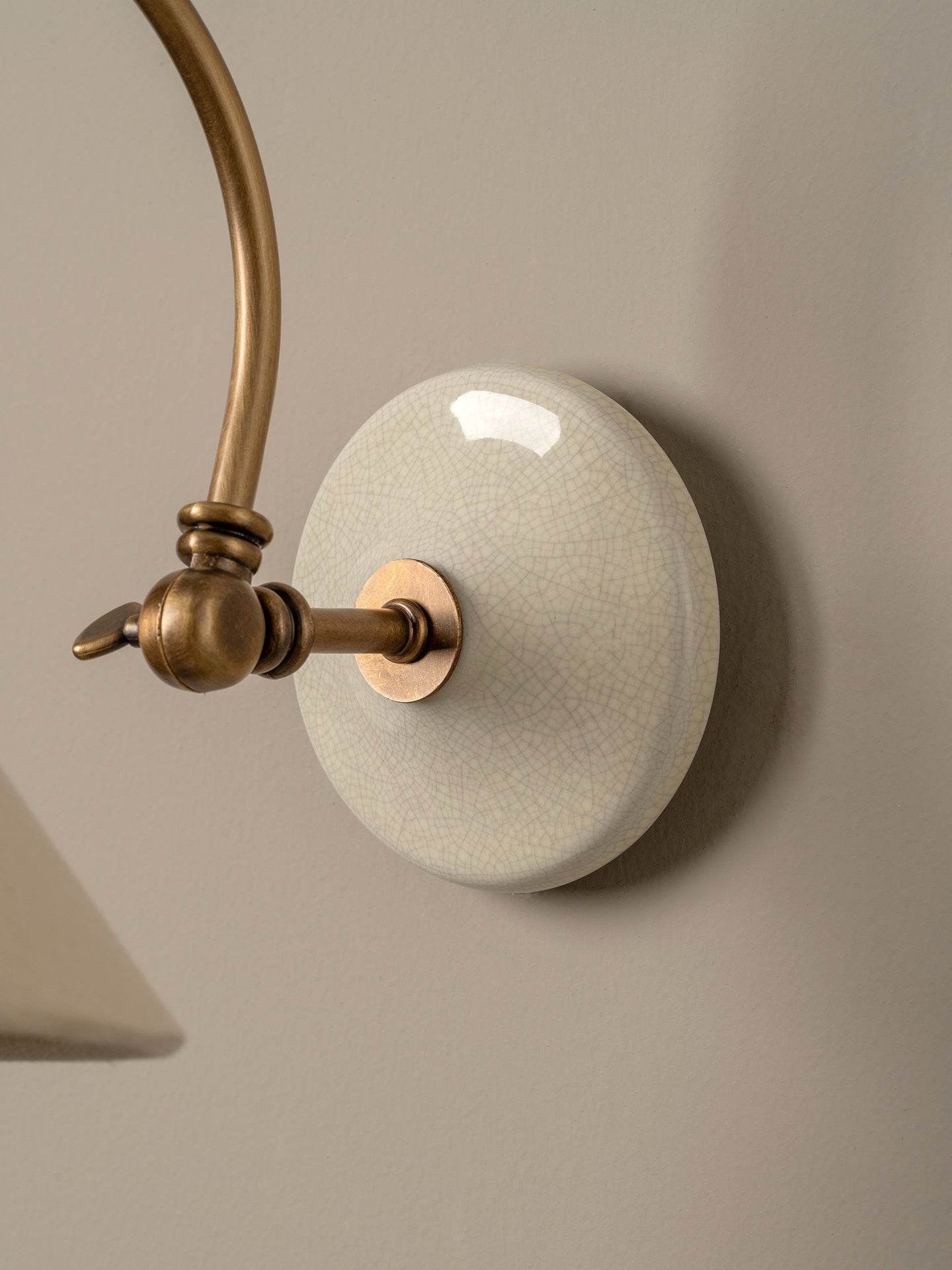 Close-up of a wall-mounted light fixture with an oval white glaze shade and curved brass-toned metal arm against a warm beige wall.