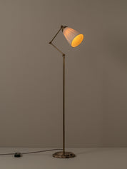 An adjustable floor lamp with a brass-finished metal frame, a pleated white shade, and a round dark marble base, shown lit against a neutral gray background.
