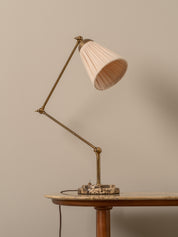Vintage-style desk lamp with a pink shade on a wooden table against a beige wall.