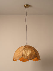 A warm-toned pendant light with a woven wicker shade hanging from a black cord and brass ceiling canopy against a plain beige wall.