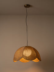 A warm-toned pendant light with a woven wicker shade hanging from a black cord and brass ceiling canopy against a plain beige wall.