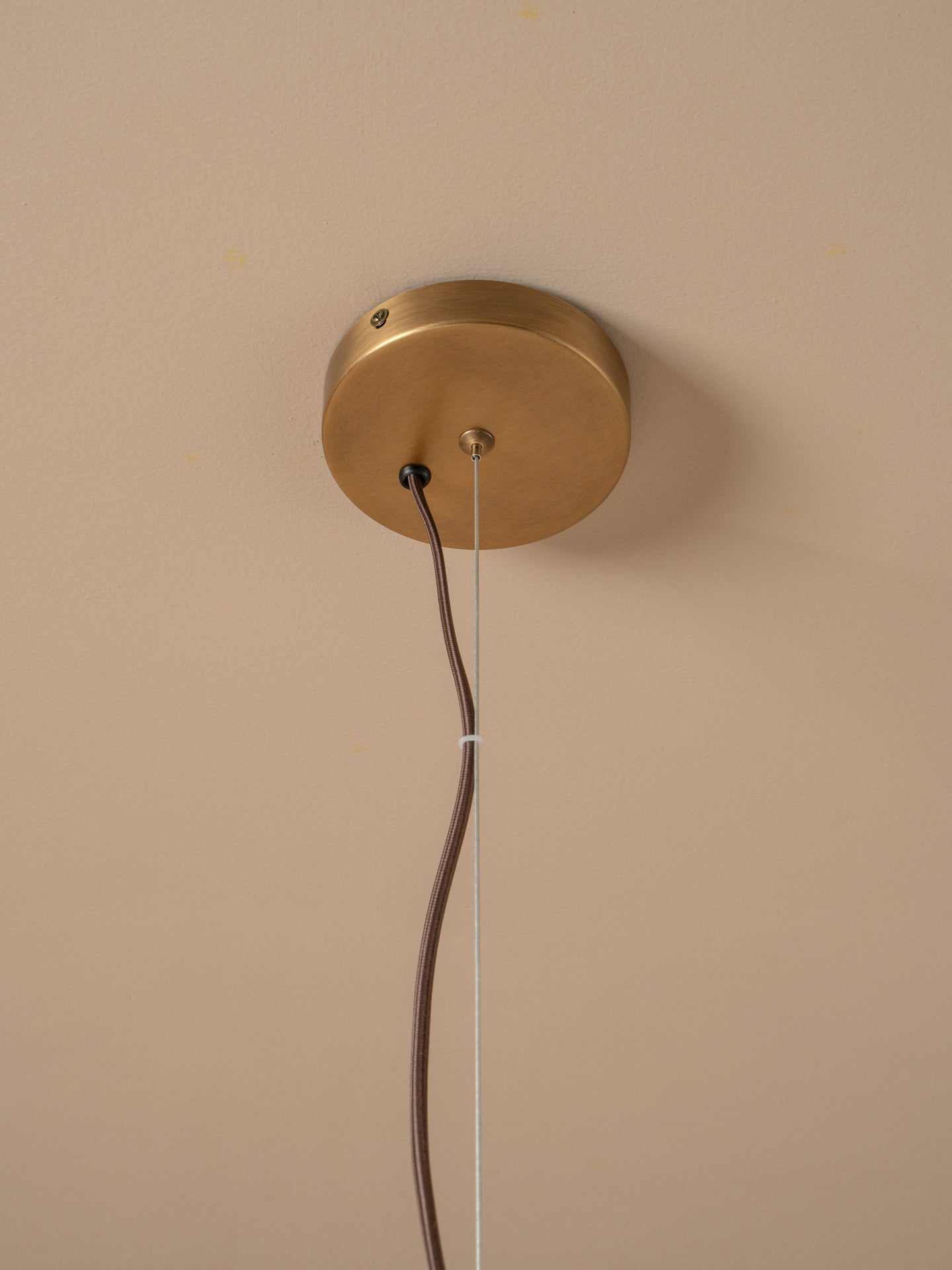A close-up of a round brass ceiling mount with a pull chain cord hanging down against a beige wall.