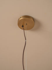A close-up of a round brass ceiling mount with a pull chain cord hanging down against a beige wall.