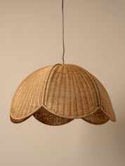 A natural woven rattan pendant lamp shade with a scalloped edge, suspended by a thin black cord against a solid beige background.