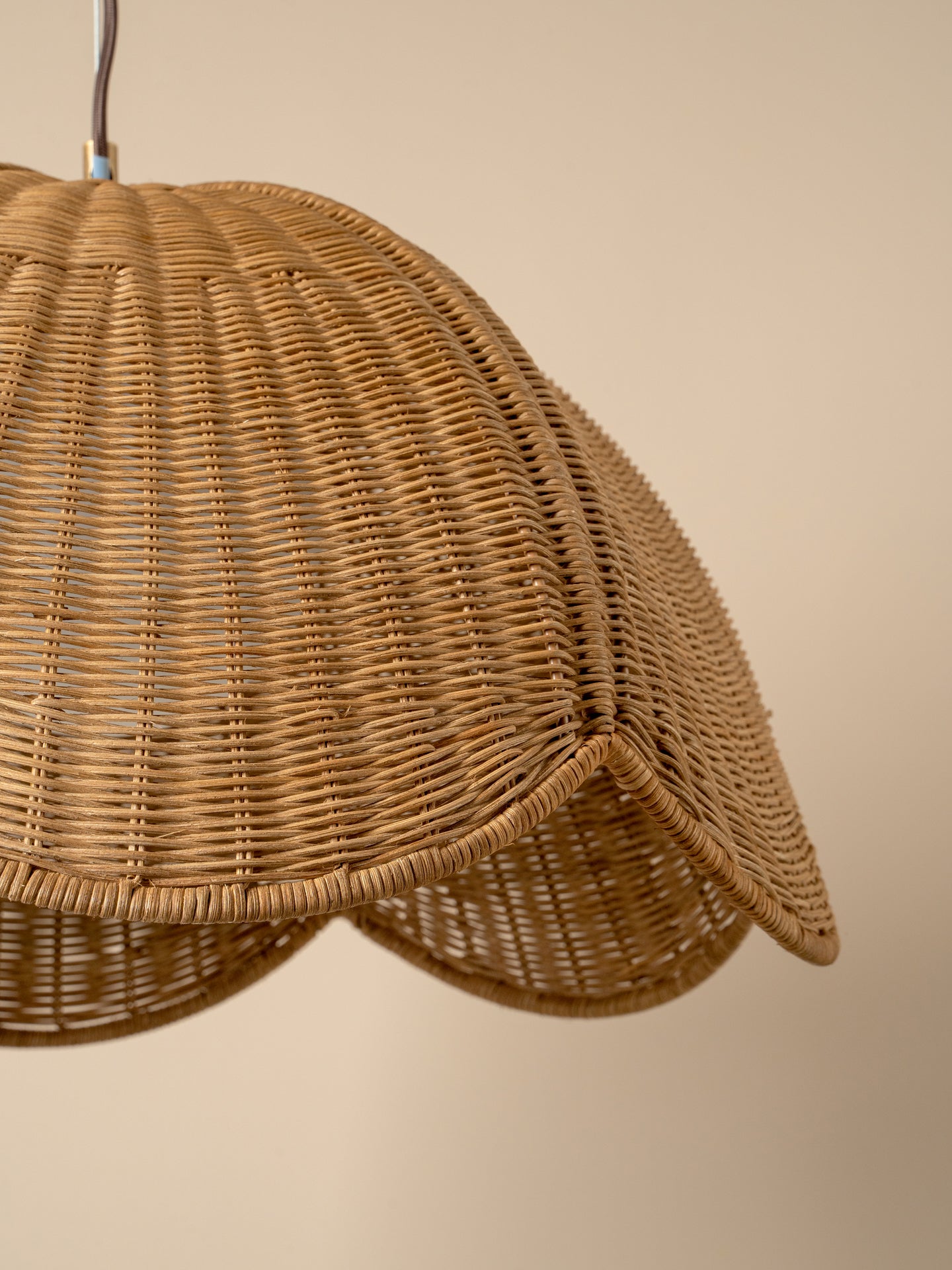 Close-up of a woven rattan pendant lamp shade in a natural tan color, showing the detailed vertical wicker pattern and scalloped lower edge against a solid beige background.