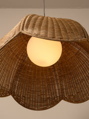A close-up of a woven rattan pendant lamp shade with a glowing warm white globe bulb inside, set against a plain beige wall.