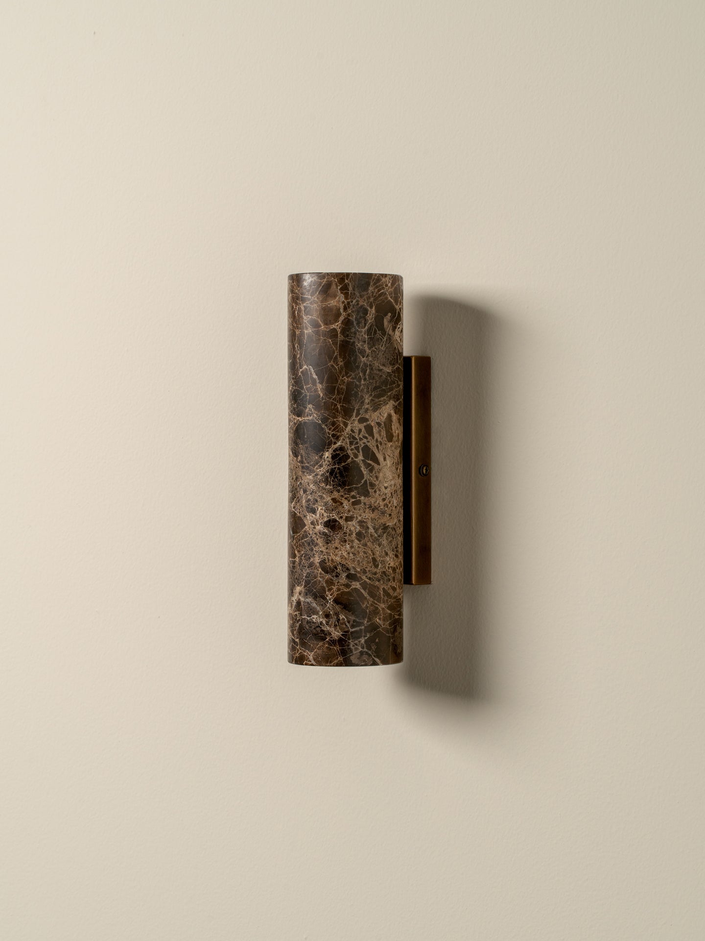 A modern cylindrical wall sconce with a dark brown and black marble textured shade and a dark metal mounting bracket, mounted on a warm beige wall.