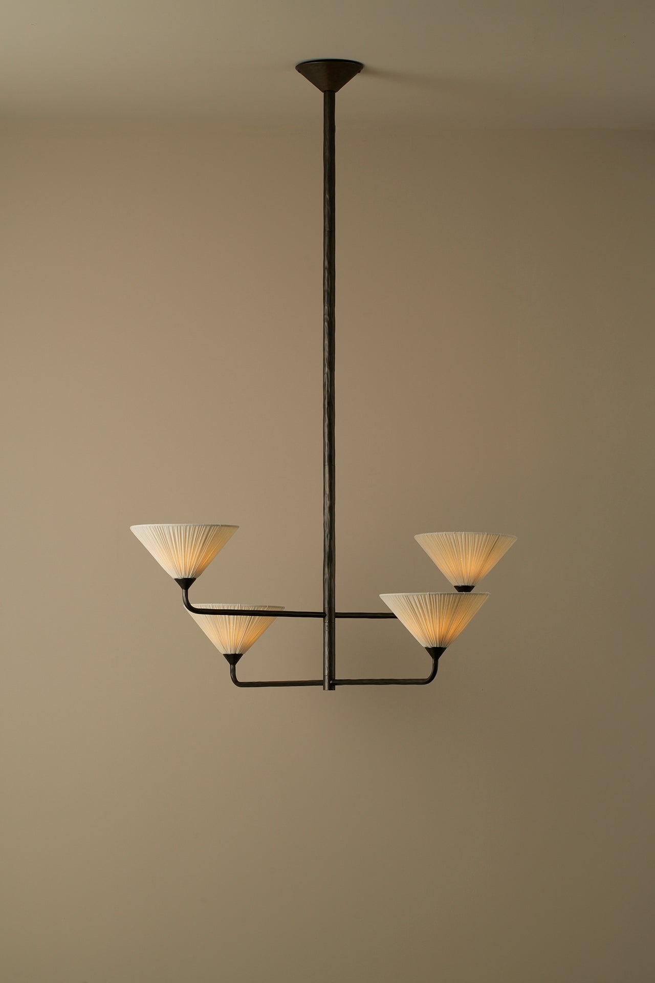 A modern 4-light chandelier with a dark metal frame and pleated cream-colored shades, suspended against a solid beige wall.