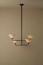 A modern 4-light chandelier with a dark metal frame and pleated cream-colored shades, suspended against a solid beige wall.