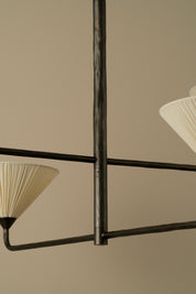 Close-up of a modern chandelier with a dark metal frame and pleated off-white fabric shades against a warm beige background.