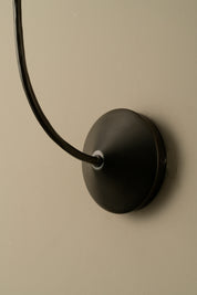 Black wall-mounted lamp with a long black cord on a beige wall.