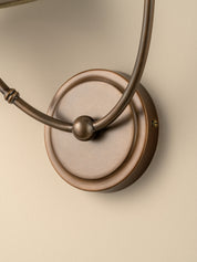 Close-up of a wall-mounted light fixture with a round bronze backplate and curved metal arms, shown against a warm beige wall.