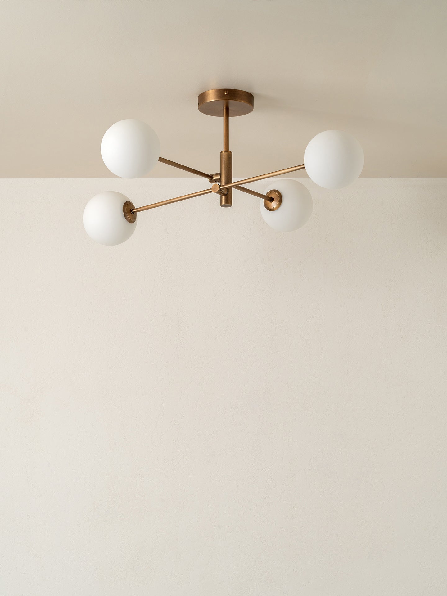 gold metal frame and white spherical glass shades, shown installed on a plain off-white ceiling.